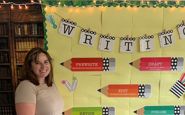 Teacher standing in front of bulletin board in a classroom