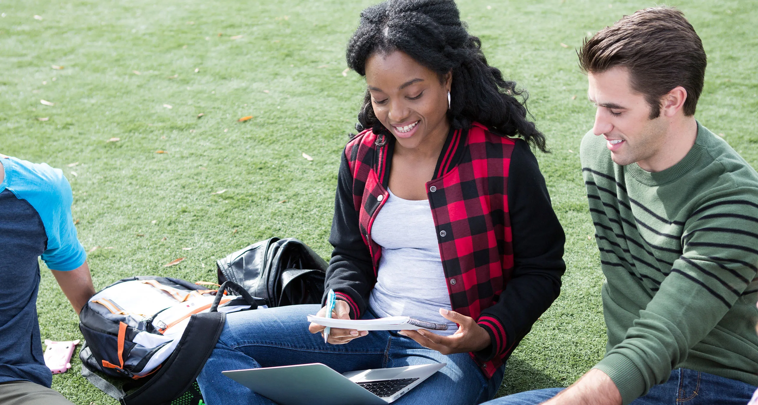 Students sitting on a patch of grass with a notebook and a laptop computer