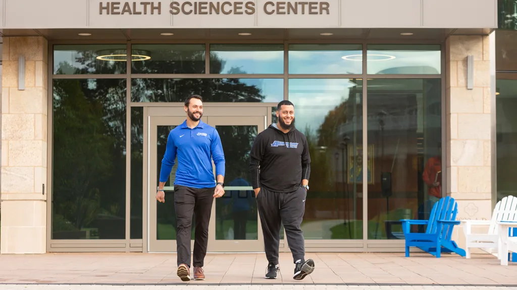Two people walking in front of the Catrambone Health Sciences Center on Assumption University's Worcester, MA campus