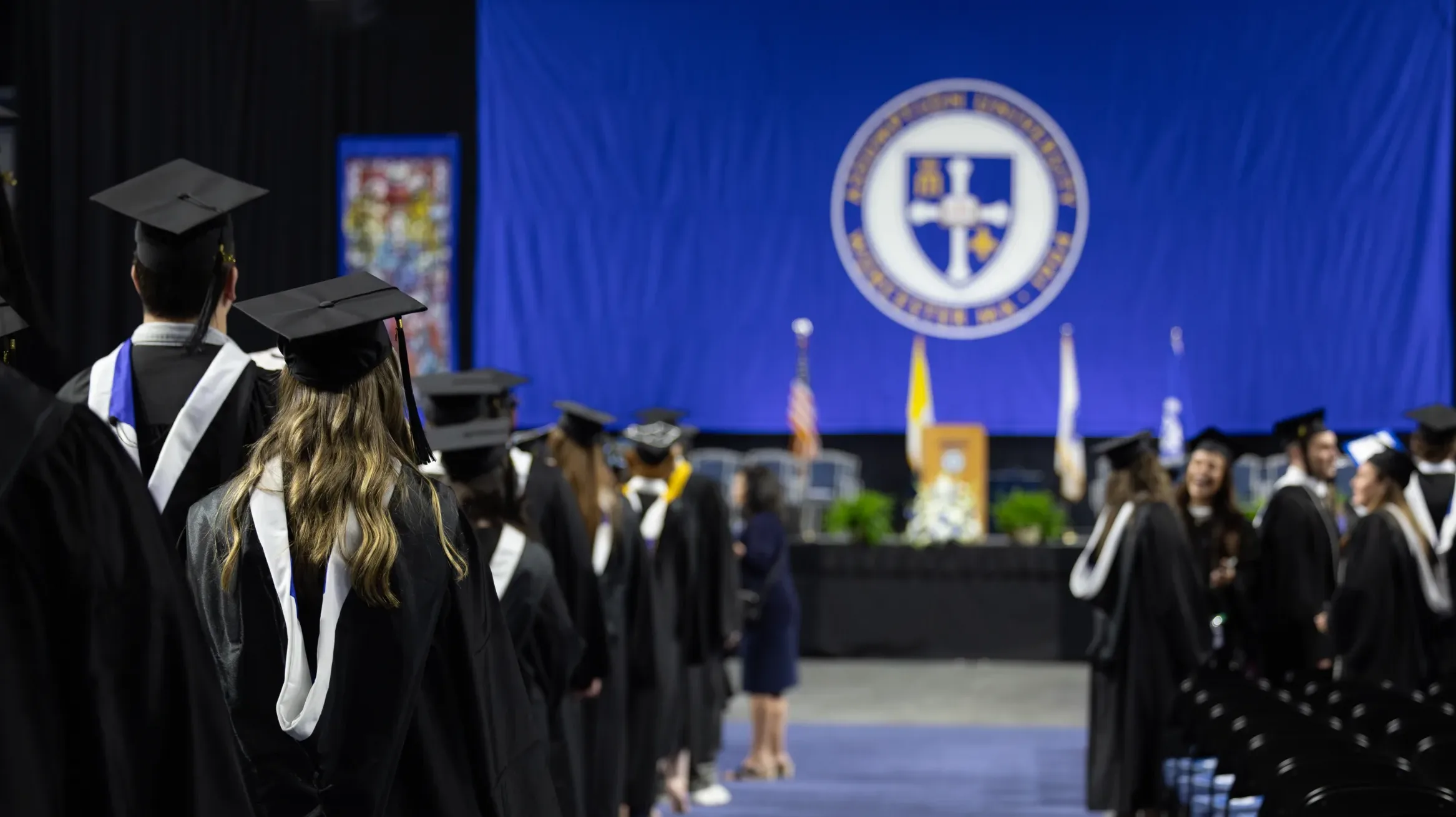 A student at the 2024 Commencement standing in front of a blue Assumption University banner